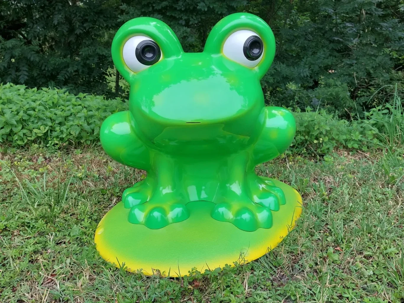 Grenouille en plastique vert brillant avec de grands yeux, posée sur un socle jaune.