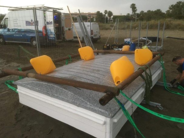 Raft en construction avec des flotteurs jaunes et des barres en bois sur une plage.