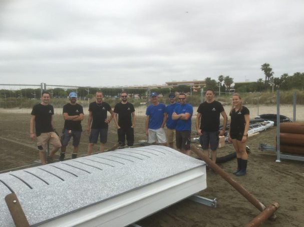 Groupe de huit personnes posant sur la plage près de canots et d'équipements nautiques.