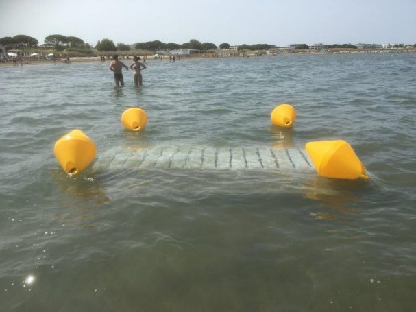 Ponton flottant en bois avec bouées jaunes, dans une eau calme, près de baigneurs.