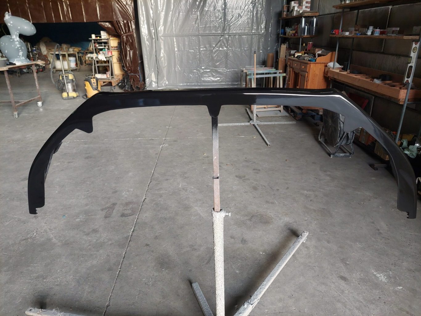 lame spoiler fabriqué, peint et vernis en polyester dans notre atelier Pièce en métal noir sur un support, dans un atelier avec divers outils en arrière-plan.